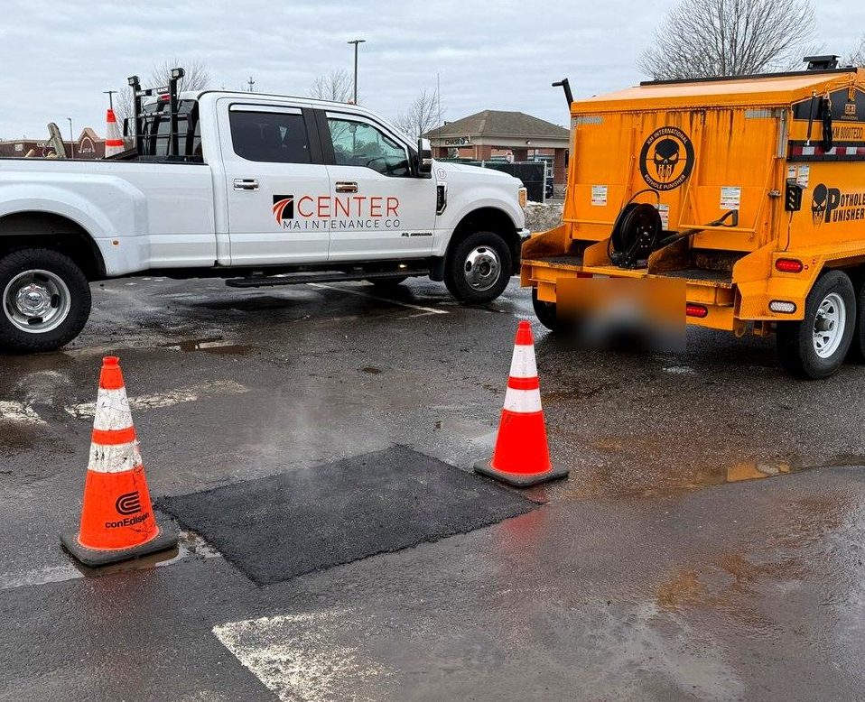 Center Maintenance Co. truck and hot-box asphalt trailer beside a freshly finished pothole patch in a Long Island parking lot